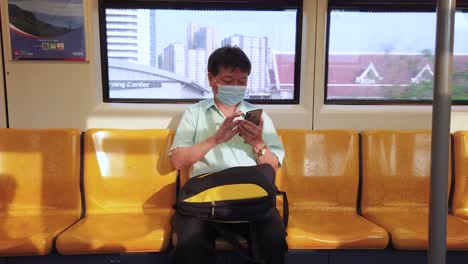 Aufnahme-Eines-Thailändischen-Mannes-In-Der-U-Bahn-Von-Bangkok,-Der-Auf-Sein-Telefon-Schaut,-Mit-Gebäuden-Im-Hintergrund,-Thailand