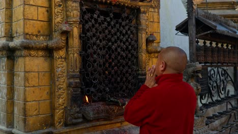 Man-praying-in-front-of-a-hindu-shrine-with-a-burning-candle-flame,-in-the-streets-of-Kathmandu,-Nepal