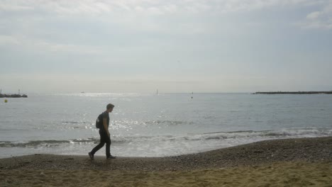 Young-man-walking-on-beach-at-Barceloneta-Beach-in-Barcelona,-Spain-on-a-cloudy-day