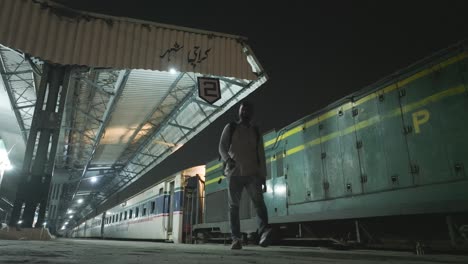 Low-angle-shot-of-man-walking-alone-along-empty-Karachi-City-Railway-station-platform-in-Karachi,-Pakistan-at-night-time