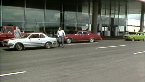 1980S-AIRPLANE-TAKING-OFF-AS-PASSENGERS-ENTER-AIRPORT-TERMINAL