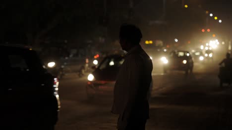 Nueva-Delhi,-India,-Hombre-Esperando-Para-Cruzar-Una-Calle-Muy-Transitada,-De-Noche