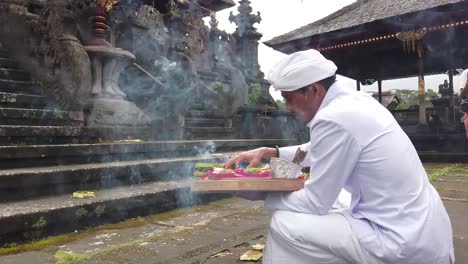 Ein-Tourist-Beobachtet-Einen-Priester,-Der-In-Einer-Balinesischen-Hindu-Zeremonie-Im-Muttertempel-Betet-Und-Die-Erde-Mit-Weihwasser-Und-Bunten-Blumenopfern-Segnet