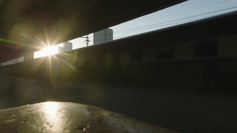 Imagen-En-ángulo-Bajo-De-Un-Tren-De-Pasajeros-Esperando-En-La-Estación-De-Tren-De-La-Ciudad-De-Karachi-Con-La-Luz-Del-Sol-Brillando-En-El-Fondo-Durante-La-Noche