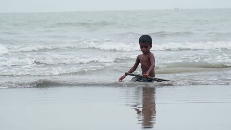 Niño-De-Bangladesh-Jugando-Solo-Con-Un-Palo-Y-Agua-En-La-Playa,-Cámara-Lenta