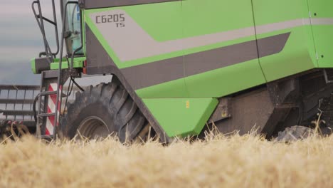 Close-up-shot-of-green-combine-harvest-harvesting-across-wheat-field-on-a-sunny-day