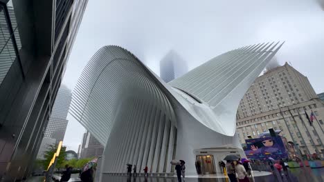 Schwenkansicht-Des-Oculus-Verkehrsknotenpunkts-Im-World-Trade-Center-In-New-York-An-Einem-Regnerischen-Tag,-An-Dem-Menschen-Mit-Regenschirmen-Vorbeigehen