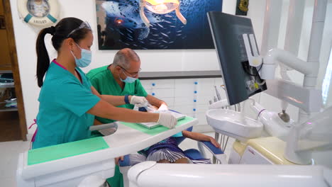 Zahnarzt-Bereitet-Sich-Darauf-Vor,-Die-Zähne-Eines-Kleinen-Mädchens-Zu-Untersuchen,-Während-Die-Krankenschwester-Die-Ausrüstung-Anpasst
