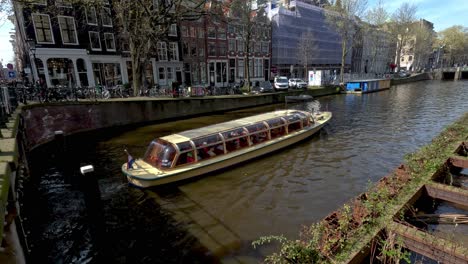 Ein-Boot,-Das-An-Einem-Schönen-Sonnigen-Tag-Einen-Kanal-Entlang-Fährt,-Als-Besichtigungstour-Durch-Die-Stadt-Amsterdam,-Niederlande