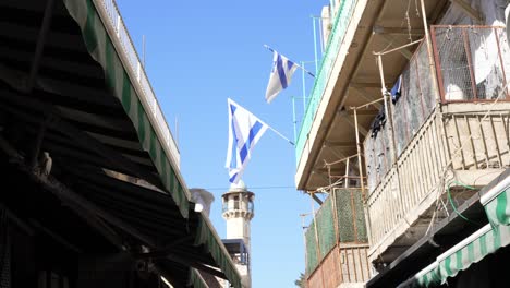 Israel's-flag-flutters-in-the-wind-in-the-center-of-the-old-city,-and-in-the-background-the-buildings