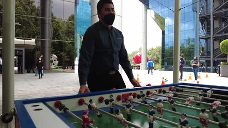 Office-colleagues-in-masks-playing-table-soccer-during-a-work-break