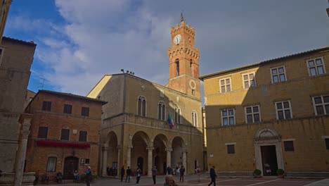 Toma-Reveladora-De-Edificios-Con-Gente-Caminando-En-La-Plaza-Renacentista-Piazza-Pio-II-En-Pienza,-Italia.