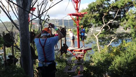 Man-with-safety-equipment-walking-along-hanging-walkways-at-an-adventure-park