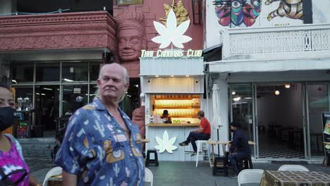 Tourists-walk-past-Thai-Cannabis-Club-kiosk-on-busy-Bangkok-street