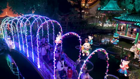 Visitors-walk-through-a-bridge-decorated-with-lights-as-they-enjoy-a-nighttime-lantern-show,-which-symbolizes-prosperity-and-good-fortune,-at-the-Wong-Tai-Sin-temple-during-the-Mid-Autumn-Festival