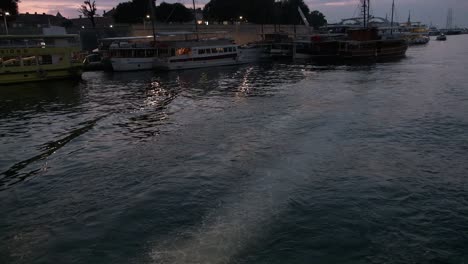 Motorboot-Rast-Nachts-Unter-Der-Brücke-Im-Hafen-Von-Zadar-Hindurch,-Während-Die-Boote-Im-Hafen-Angedockt-Sind