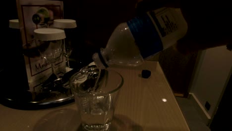 Mann-Gießt-Wasser-Aus-Einer-Plastikflasche-In-Ein-Glas-In-Einem-Hotelzimmer-Auf-Dem-Schreibtisch-Oder-Tisch