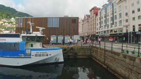Ferry-Atracado-En-El-Puerto-De-Bergen-En-Noruega-Con-Gente-Caminando-De-Compras-A-Lo-Largo-Del-Paseo-Marítimo
