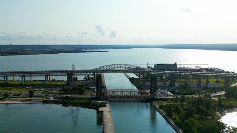 Panoramic-aerial-overlooking-Burlington-Bay-Canal-Lift-Bridge-Queen-Elizabeth-Highway-summer-day-clear-sky-light-traffic-stunning-beaches-lush-green-parks-vehicles-and-boats-crossing-during-rush-hour