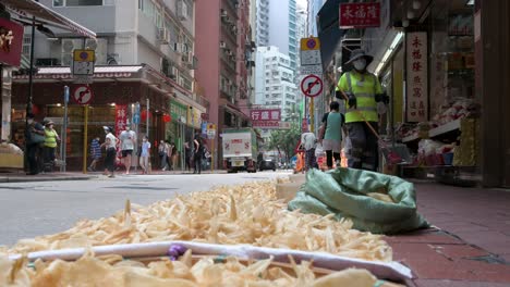 Pedestrians-walk-past-seafood-for-sale-left-to-dry-on-the-street-sidewalk,-a-common-ingredient-in-Chinese-cuisine,-cooking,-and-traditional-medicine