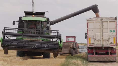 Slow-motion-shot-of-harvester-combine-pouring-grain-into-truck-on-field-on-a-cloudy-day