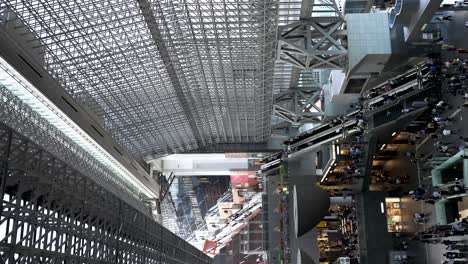 Blick-Hinunter-Auf-Das-Belebte-Atrium-Des-Bahnhofs-Kyoto-Mit-Menschen,-Die-Vom-Westende-Aus-Auf-Der-Rolltreppe-Auf-Und-Ab-Gehen