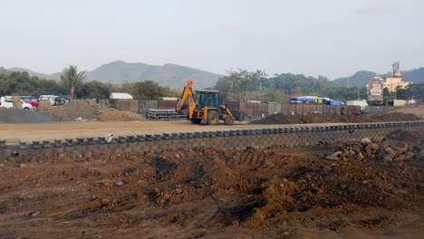 Amidst-the-hustle-and-bustle-of-India's-busy-road-traffic,-a-JCB-excavator-tirelessly-works-near-the-roadside,-contributing-to-road-construction-efforts