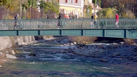 Pedestrians-walk-across-a-footbridge-over-the-river-Passer-in-Meran---Merano,-South-Tyrol,-Italy