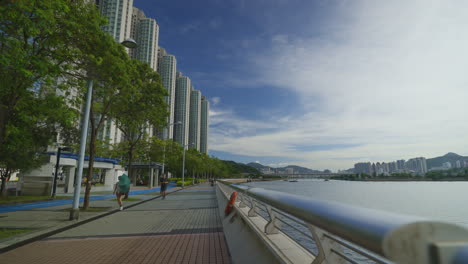 Pov-dolly-walk-on-promenade-in-Hong-Kong-City-during-sunny-day-with-skyscraper-and-river-bay---Jogging-during-sunrise-in-the-morning