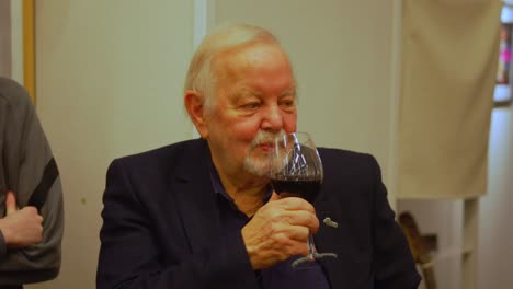 Older-well-dressed-white-man-with-beard-drinking-from-a-full-glass-of-red-wine