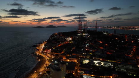 Aerial-view-orbiting-a-illuminated-hill-on-the-coast-of-Mazatlan,-vibrant-evening-in-Mexico