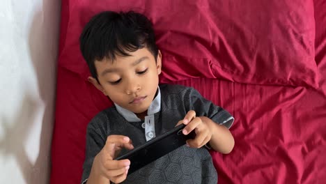 A-4-year-old-asian-boy-playing-games-on-his-smartphone-while-lying-in-bed