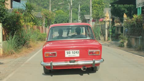 Klassisches-Rotes-Auto,-Das-In-Die-Ferne-Mit-Grünen-Waldbergen-In-Thailand-Fährt