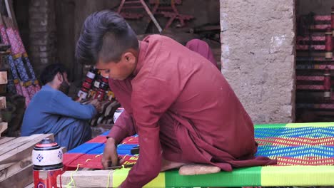 Niño-Trabajador-Usando-Hilo-Para-Tejer-Alrededor-De-Charpai,-Una-Cama-Tejida-Tradicional-En-Sindh,-Pakistán