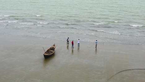 Aerial-View-Of-Group-Of-Male-Friends-Standing-Beside-Empty-Fishing-Boat-On-Kuakata-Beach
