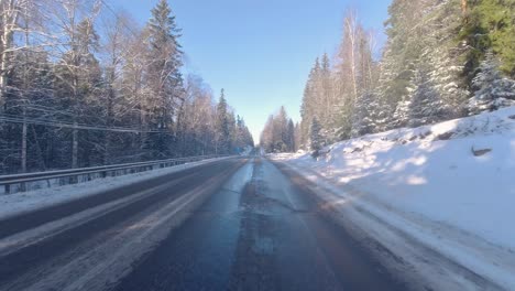 As-the-car-travels-along-the-road,-beside-it-stands-snow-covered-pine-trees,-creating-a-picturesque-winter-scene