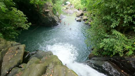 Balinese-local-Guide-cliff-jump-into-natural-Pool-of-Kroya-Waterfall-amid-lush-tropical-forest-of-Aling-Aling-falls,-Bali