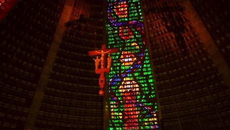 Tilt-up-of-the-interior-of-the-Metropolitan-Cathedral-of-Rio-de-Janeiro,-cross-of-Christ-in-the-center-and-giant-colorful-stained-glass-windows-illuminated-by-external-daylight