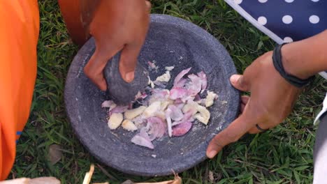 Close-up-of-woman-using-a-mortar-and-pestle-to-grind-up-fresh-garlic-and-onion-ingredients-for-lunch-preparation-in-outdoor-environment