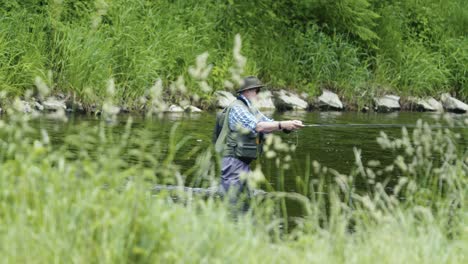 A-man-wearing-a-hat-and-sunglasses-stands-in-the-river,-engaged-in-the-art-of-fly-fishing