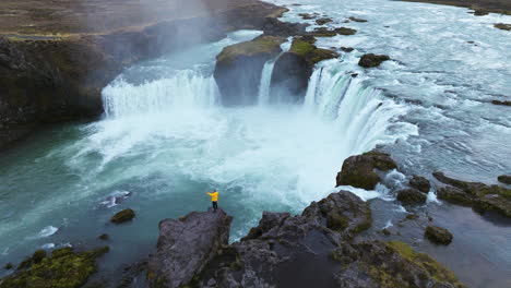 Aerial-View-Of-A-Man-On-The-Edge-Of-A-Cliff-Near-Godafoss-Waterfall-In-Iceland