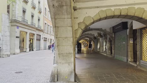 On-the-streets-of-Annecy,-stone-arched-passage-and-pedestrians-in-summer