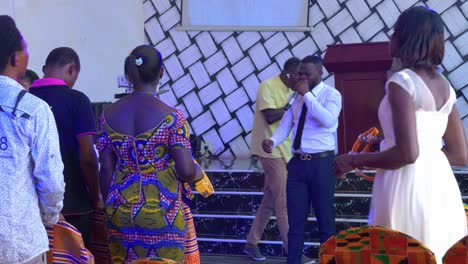 Two-African-young-men-singing-effusively-with-a-microphone-while-women-dance