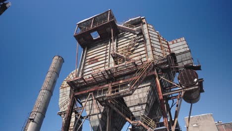 An-old,-rusted-and-dilapidated-former-electrostatic-precipitator-with-a-towering-chimney-under-a-clear-winter-blue-sky