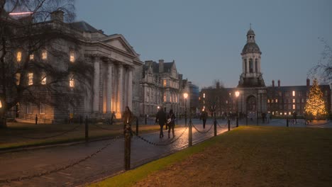 Gente-Caminando-Afuera-Del-Edificio-Del-Trinity-College-Con-El-Campanario-Por-La-Noche-En-Dublín,-Irlanda