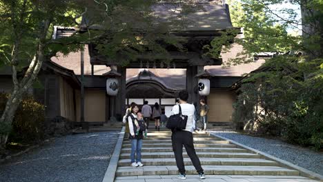 Marido-Japonés-Tomando-Una-Foto-De-Su-Esposa-Sosteniendo-A-Un-Bebé-En-Un-Portabebés-Frente-A-Las-Escaleras-Que-Conducen-Al-Templo-Budista-En-Koyasan