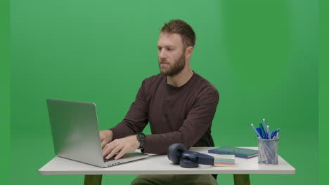Uoung-Caucasian-man-is-using-his-laptop-in-a-frontal-view,-captured-in-a-portrait-shot-with-a-green-screen-or-chroma-key