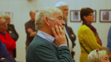 White-elderly-gentleman-supports-his-face-with-his-hand-during-art-fair-opening