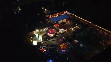 Illuminated-fairground-festival-in-neighbourhood-pub-car-park-at-night-aerial-view