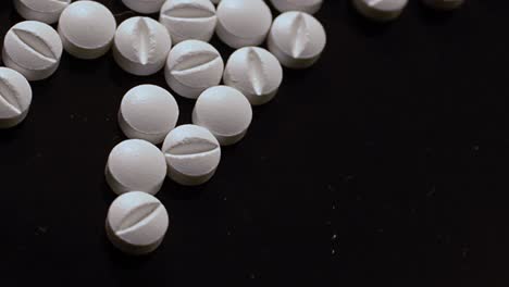 Drug-addiction---white-pills-sprinkled-on-a-black-surface-and-handled-illegally